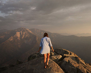 A woman walks on a mountain top at sunset